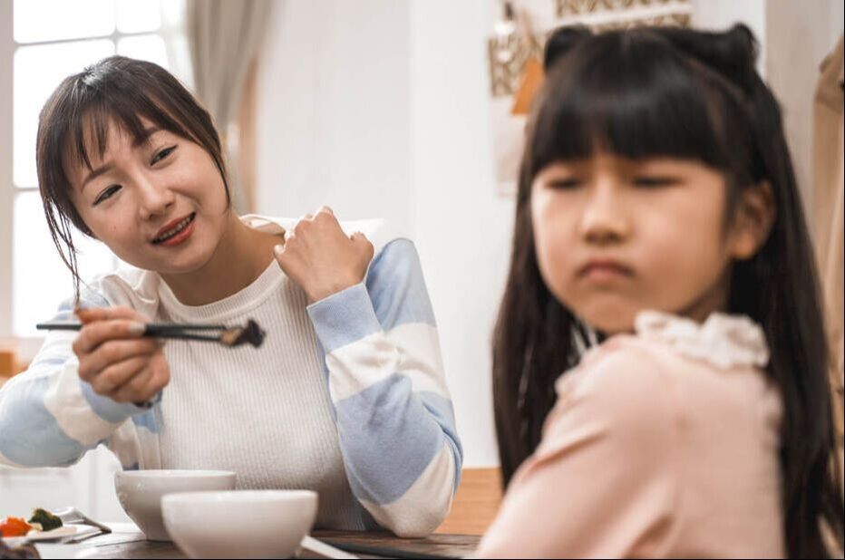 Mother offers frowning daughter food during mealtime