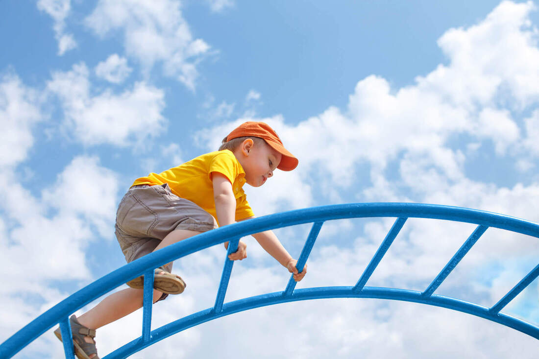 Toddler climbs a jungle gym in front of a blue sky